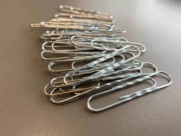 Shiny metal paper clips on a desktop with stationery in a business office. Close view.