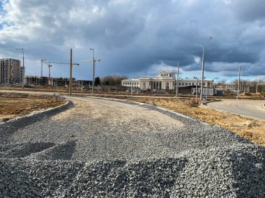 Büyük gri taşlar, endüstriyel yol inşaatından kalma molozlar ve şantiyede vinçleri olan yeni binalar..