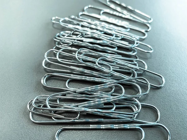 Shiny metal paper clips on a desktop with stationery in a business office. Close view.