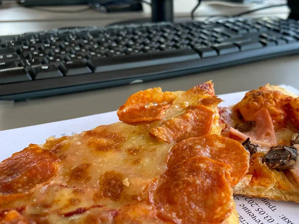 Desktop mix with office gadgets, supplies and pizza on a wooden office table background. View from above.