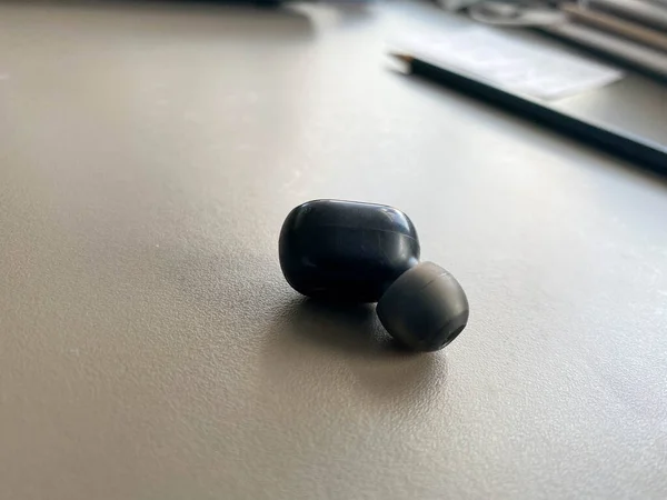 桌上放着一个用于听音乐的黑色小塑料无线蓝牙耳机 — 图库照片