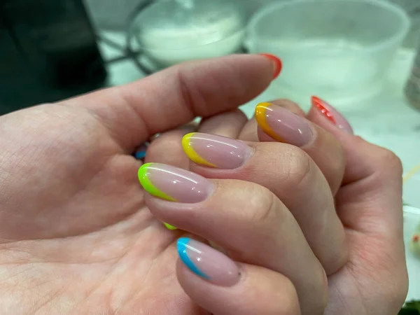 Beautiful multicolored women's manicure fashionable stylish french on the fingers with gel varnish of different colors of the rainbow transparent yellow red green blue. Stylish nail design.