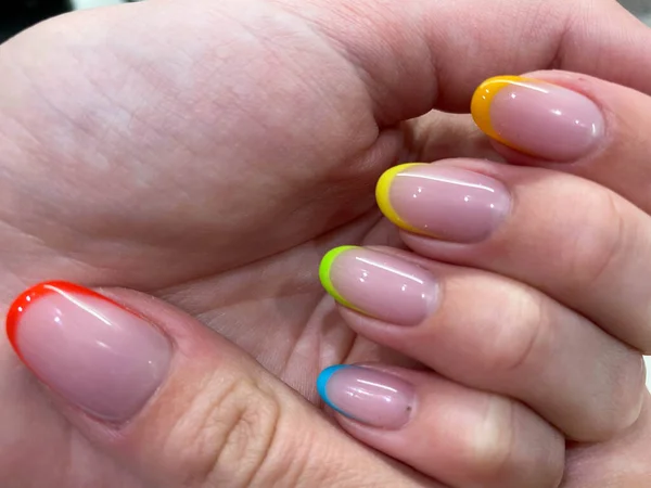 Beautiful multicolored women's manicure fashionable stylish french on the fingers with gel varnish of different colors of the rainbow transparent yellow red green blue. Stylish nail design.
