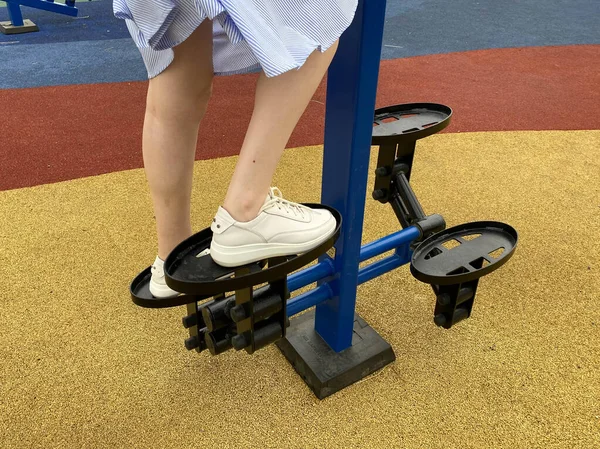 A woman goes in for sports on a new modern blue fitness leg trainer for walking and running on an outdoor workout site.