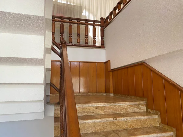 Luxury interior: marble staircase with wrought-iron railing and wooden handrail.