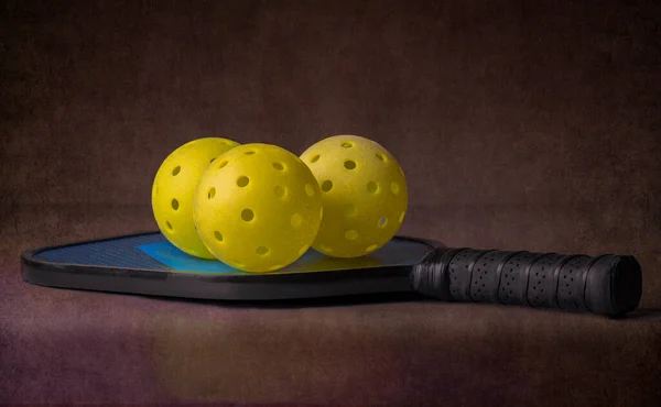Pickleball raketinde üç wiffleball topu. Karanlık bir arka planda.