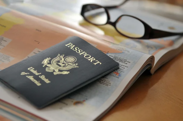 Paspoort en bril op de atlas — Stockfoto