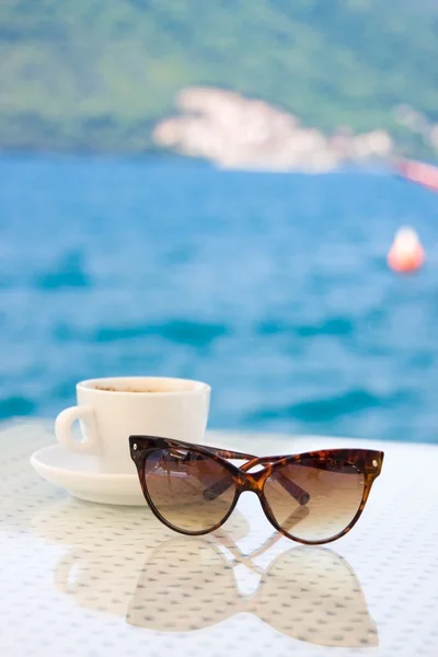 Sunglasses and cup of coffee against sea — Stock Photo, Image
