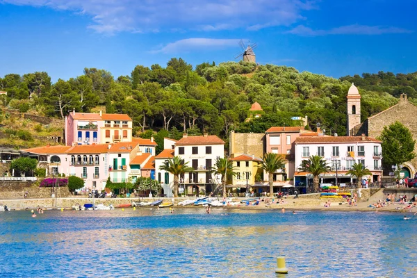 COLLIOURE, FRANCE - JULY 5, 2016: Beach hotels in Collioure village with a windmill at the top of the hill, Roussillon, Vermilion coast, Pyrenees Orientales, France — Stock Photo, Image