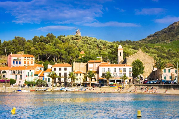 Collioure, Francja - 5 lipca 2016: Hotele Beach w miejscowości Collioure z wiatrakiem u góry hill, Roussillon, Vermilion wybrzeża, Pyrenees Orientales, Francja — Zdjęcie stockowe