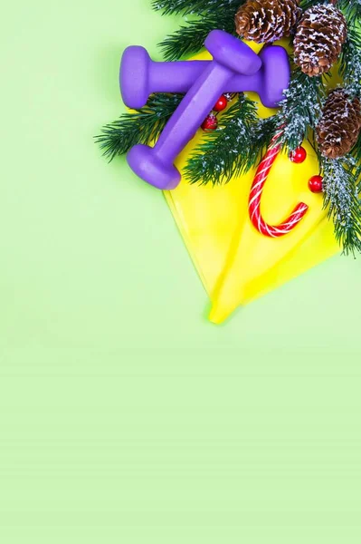 クリスマスのフィットネス 健康的でアクティブなライフスタイルグリーティングカードのコンセプト 紫色のダンベル 黄色のゴムバンド 緑のキャンディとモミの木 ストック画像