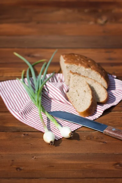 Rye bread, onion and knife on wood, outdoor. Focus on onion — Stock Photo, Image