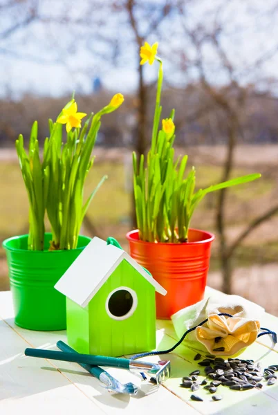Πράσινο πουλί σπίτι και Νάρκισσος σε γλάστρες, φτυάρι και σπόρους κατά κήπο άνοιξη — Φωτογραφία Αρχείου