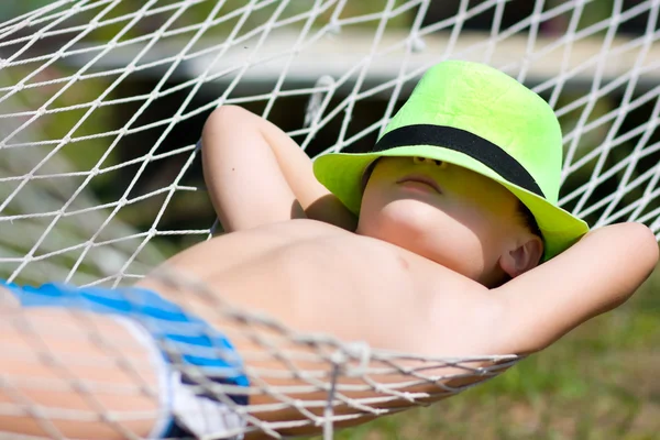 Niño feliz en hamaca en el jardín. Concéntrate en sombrero —  Fotos de Stock