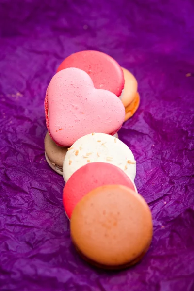 Macarons coloridos franceses com corações em fundo violeta — Fotografia de Stock