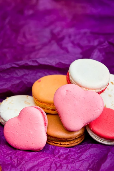 Macarons coloridos franceses com corações em fundo violeta — Fotografia de Stock