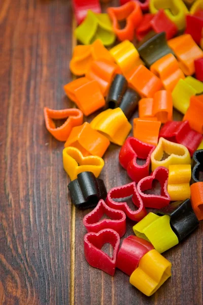 Heart-shaped pasta on wood table. Focus on red — Stock Photo, Image