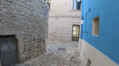 Casamassima, İtalya 'da karakteristik dar bir sokakta yürümek. Ünlü Mavi Köy. Videoda taş evler, geleneksel Akdeniz mimarisi ve bu tarihi merkezi eşsiz kılan ikonik parlak mavi duvar yer alıyor..