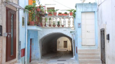 Kemerli taştan bir geçit, saksı bitkileriyle geleneksel balkonlar ve tarihi Akdeniz mimari unsurlarının karışımının yer aldığı büyüleyici mavi boyanmış bir sokak. Bu resim sahnesi eski Casamassima kasabasına ait.