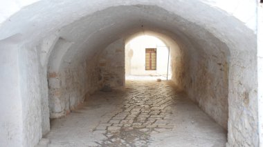 Kemerli tavanı ve parke taşlı zemini olan beyaz boyalı taş bir tünel. Ahşap pencereli güneşli bir cepheye doğru açılıyor. Bu geleneksel geçit Güney İtalya 'nın mavi köyü olarak bilinen Casamassima' nın tarihi merkezinin bir parçasıdır..