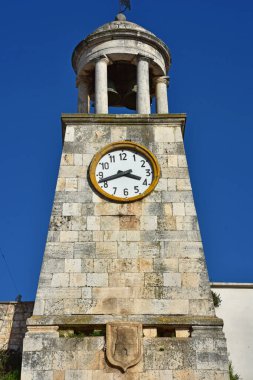 Casamassima 'daki tarihi taş saat kulesine yakından bakın. Büyük yuvarlak saat yüzlü, kemerli çan kulesi ve yıpranmış taş bloklar var. Parlak mavi gökyüzü kuleleri güzelleştirir mimari güzelliği ve zamansız karakteri.