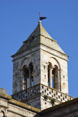 Casamassima 'daki tarihi bir çan kulesinin yakından görüntüsü, kemerli açılışlar, eski duvarcılık ve geleneksel piramit çatısı. Sıcak ışık ve açık mavi gökyüzü bu antik yapının mimari güzelliğini vurguluyor..