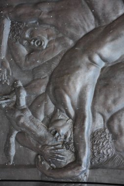 Anlamlı insan figürlerini ve dramatik heykel şekillerini gösteren bronz levreğin yakın çekimi. Bu sembolik kompozisyonda desenli metal yüzey duygusal yoğunluğu, sanatsal zanaatkarlığı ve karmaşık ayrıntıları vurgular..