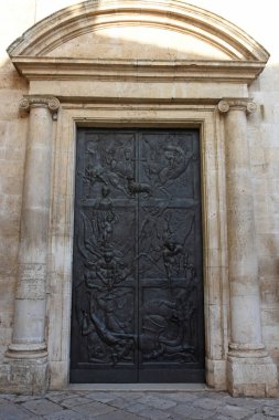 Taş sütunlarla çerçevelenmiş bronz bir kilise kapısı ve Casamassima 'da kemerli klasik bir yapı. Mavi Köy 'de detaylı yardım çalışmaları ve tarihi mimari.