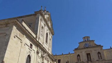 Lecce, İtalya. Şehir merkezindeki katedral cephesini ve çan kulesini gösteren yavaş çekim. Barok dini mimarisi ve İtalya 'nın güneyindeki tarihi yapılar açık mavi gökyüzünün altında..