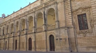 Lecce, İtalya. Şehir merkezinde kemerler ve taş mimari ile tarihi bir saray cephesinin yavaş çekim sahnesi. Güneşli bir günde güney İtalya 'da barok tarzı yapı ve mimari ayrıntılar.