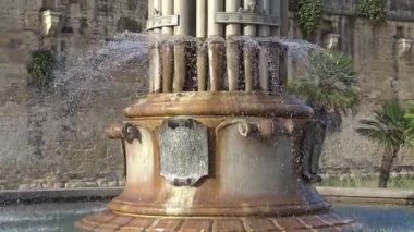 Lecce, İtalya. Şehir merkezindeki taş elementlerin üzerinden akan suyun olduğu devasa bir çeşmenin altından üstüne yavaş bir eğim atışı. Güney İtalya 'da güneşli bir günde mimari ve sanatsal detaylar.