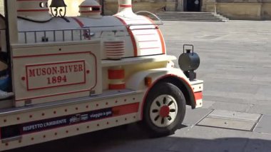 Lecce, İtalya. Şehir merkezindeki tarihi bir meydandan geçen bir turist treninin sabit kamera görüntüsü. Güneşli bir günde güney İtalya 'da gezi aracı, kentsel yaşam ve turizm faaliyetleri. Sadece editör kullanımı.