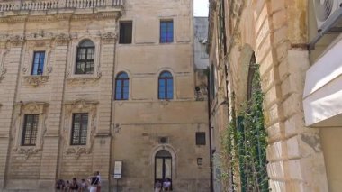 Lecce, İtalya. Şehir merkezinde turistlerin gezip dolaştığı tarihi bir saray cephesinin yavaş çekim sahnesi. Güneşli bir günde güney İtalya 'da barok mimari, kentsel yaşam ve turizm.
