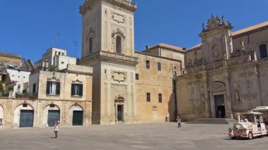 Lecce, İtalya. Tarihi bir çan kulesinin ve şehir merkezindeki binaların yavaş çekim görüntüleri. Dini mimari ve İtalya 'nın güneyinde güneşli bir günde bir dönüm noktasının taş detayları.