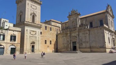 Lecce, İtalya. Şehir merkezindeki katedralin ve ana meydanın sabit kamera görüntüsü ve birkaç kişi yürüyor. Barok dini mimarisi ve güney İtalya 'daki tarihi yapılar güneşli bir günde.