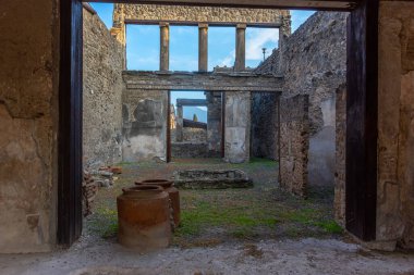 İtalya 'nın Pompeii arkeoloji sahasındaki taş duvarlar, sütunlar ve saklama kavanozlarıyla antik bir Roma evinin içini incele. Roma günlük yaşamını ve mimarisini gösteren muhafaza edilmiş iç alan.