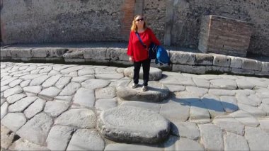 Pompeii, İtalya 15 Ekim 2019. Pompeii arkeoloji sahasındaki orijinal taş kaldırımda duran bir kadın turist, M.Ö. 79 yılında Vesuvius Dağı 'nın patlaması sonucu gömülü Roma sokaklarını ve kentsel altyapısını sergiliyor..