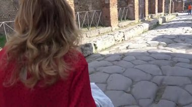 Pompeii 'de taş döşeli antik bir cadde boyunca yürüyen bir turist, eski şehrin korunmuş yol sistemini ve kentsel yerleşim planını vurguluyor..
