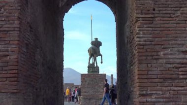 Zaman aşımı, Pompei 'deki bir Roma tuğla kemerinde yürüyen turistlerin arka planda çerçevelenmiş bir binicilik heykeliyle antik kalıntılar ve modern ziyaretçiler arasındaki etkileşimi vurguluyor..