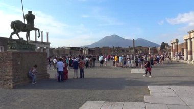 Zaman atlaması, Pompei 'nin arkeolojik bölgesinde seyahat eden turistlerin arka planda Vesuvius Dağı ile antik harabeler ve modern turizm arasındaki zıtlığı vurguluyor..