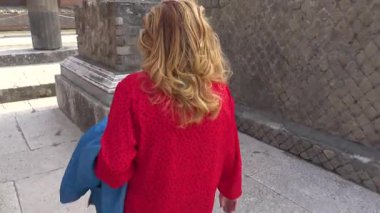 Pompei 'deki antik Roma harabelerini gözlemleyen turist, antik kentin korunmuş kentsel manzarasını gösteren taş yapıların ve sütunların yanında duruyordu..