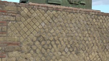 Pompei 'de, antik Roma kültürünün sanatsal ve sembolik unsurlarını vurgulayan bir at ve savaşçı motifi ile bronz bir kabartma içeren eğik bir duvar manzarası.