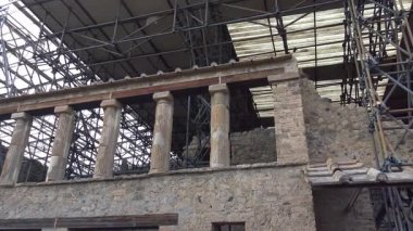 Pompei 'de restore altındaki antik bir Roma evinin manzarası, sütunları, taş duvarları ve arkeolojik alandaki koruma çalışmalarını ön plana çıkaran koruyucu iskeleleri.