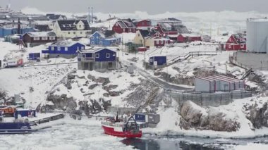 Grönland 'da kayalık sahillerde balıkçı tekneleri ve evleri olan renkli Kuzey Kutup köyü, kış kutup manzarası, soğuk iklim, uzak yerleşim ve deniz kenarındaki geleneksel kuzey yaşam tarzı.