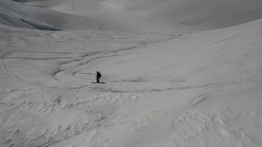 Uçsuz bucaksız bir dağ yamacında kavisli izler oyan bir kayakçının geniş hava manzarası. Minimum kış manzarası, ölçek, özgürlük ve alp macera kavramı.
