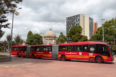 BOGOTA, COLOMBIA - Üç vagon Transmilenio otobüsü Gabriel Garcia Marquez gazeteci parkını geçiyor Simon Bolivar tapınağı ve ofis binaları güneşli bir günde şehir merkezinde