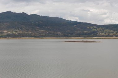 Bulutlu dağlarda yeşil dağları olan mavi bir laktenin ortasındaki mini adaya yakın..