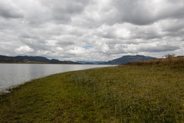 Mavi bir gölün yanında yeşil çimenler ve arka planda bulutlu gri gökyüzü. Kamp ve seyahat kavramı