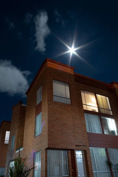 Stunning night photography of brick house with lights on and starry night with full moon like a star.