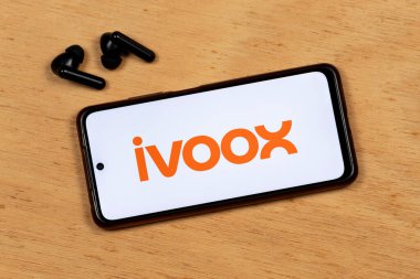 Akıllı telefon ekranının makro fotoğrafı ahşap arka planda kablosuz kulaklıkla portakal uygulamalı logoyu gösteriyor.